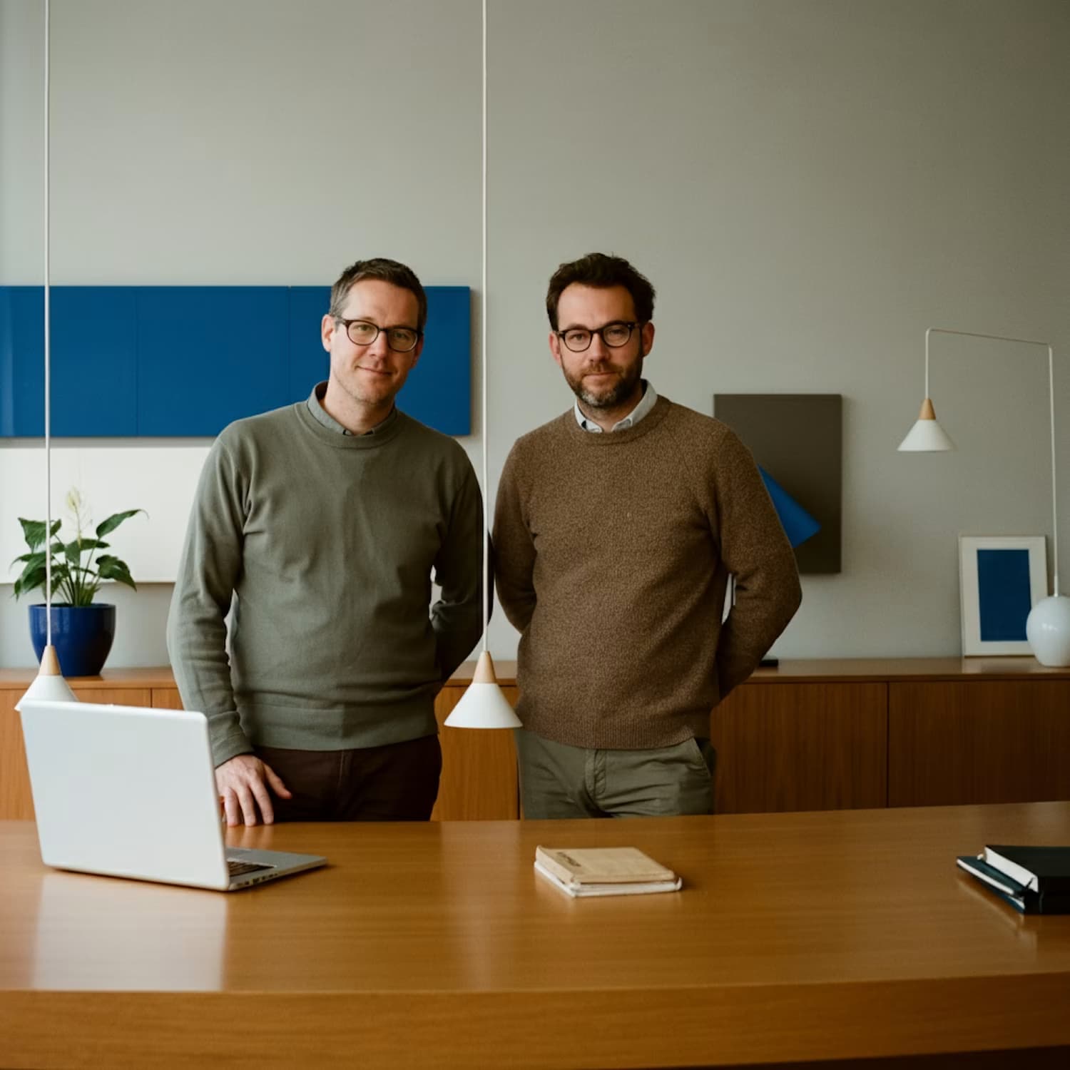 Deux collègues posent debout derrière un bureau en bois