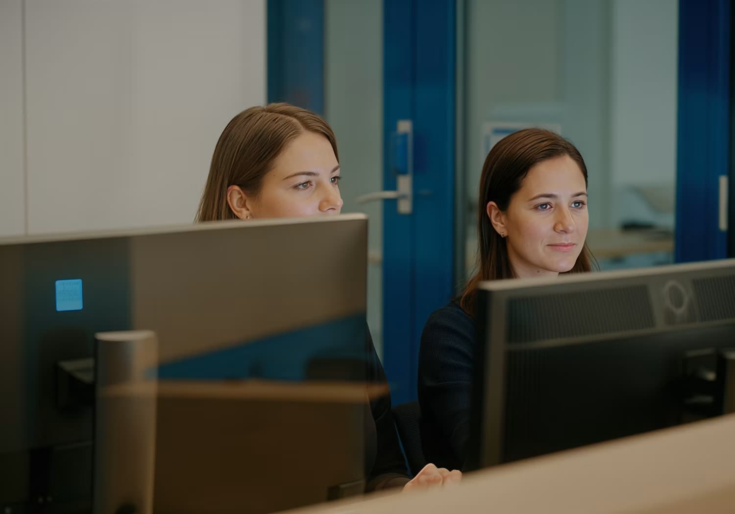 Deux collègues concentrées devant leurs écrans dans un bureau vitré