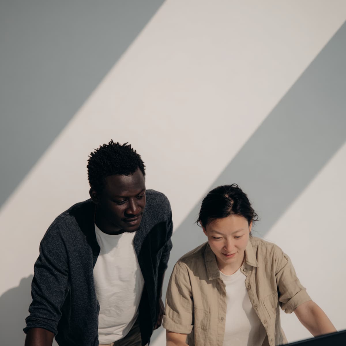 Deux collègues collaborent dans un espace lumineux, jeux d’ombres sur le mur