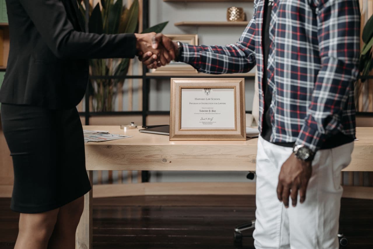 Une poignée de main devant un diplôme encadré posé sur un bureau