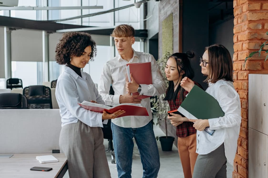 Quatre collègues échangent en consultant ensemble des documents