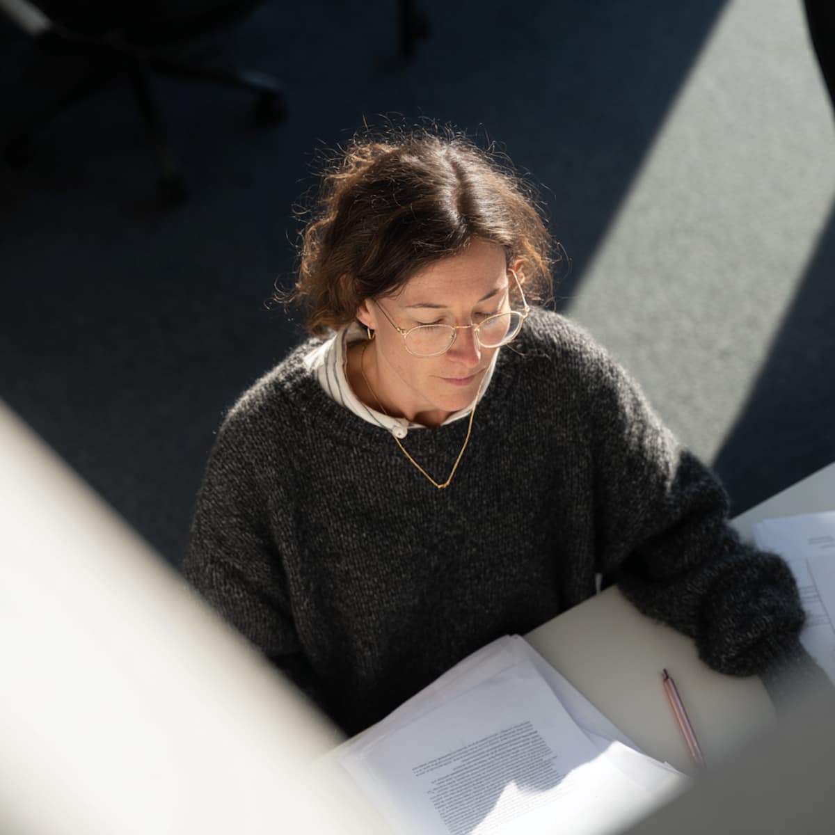 Une salariée à lunettes relit des documents à son bureau, vue en plongée