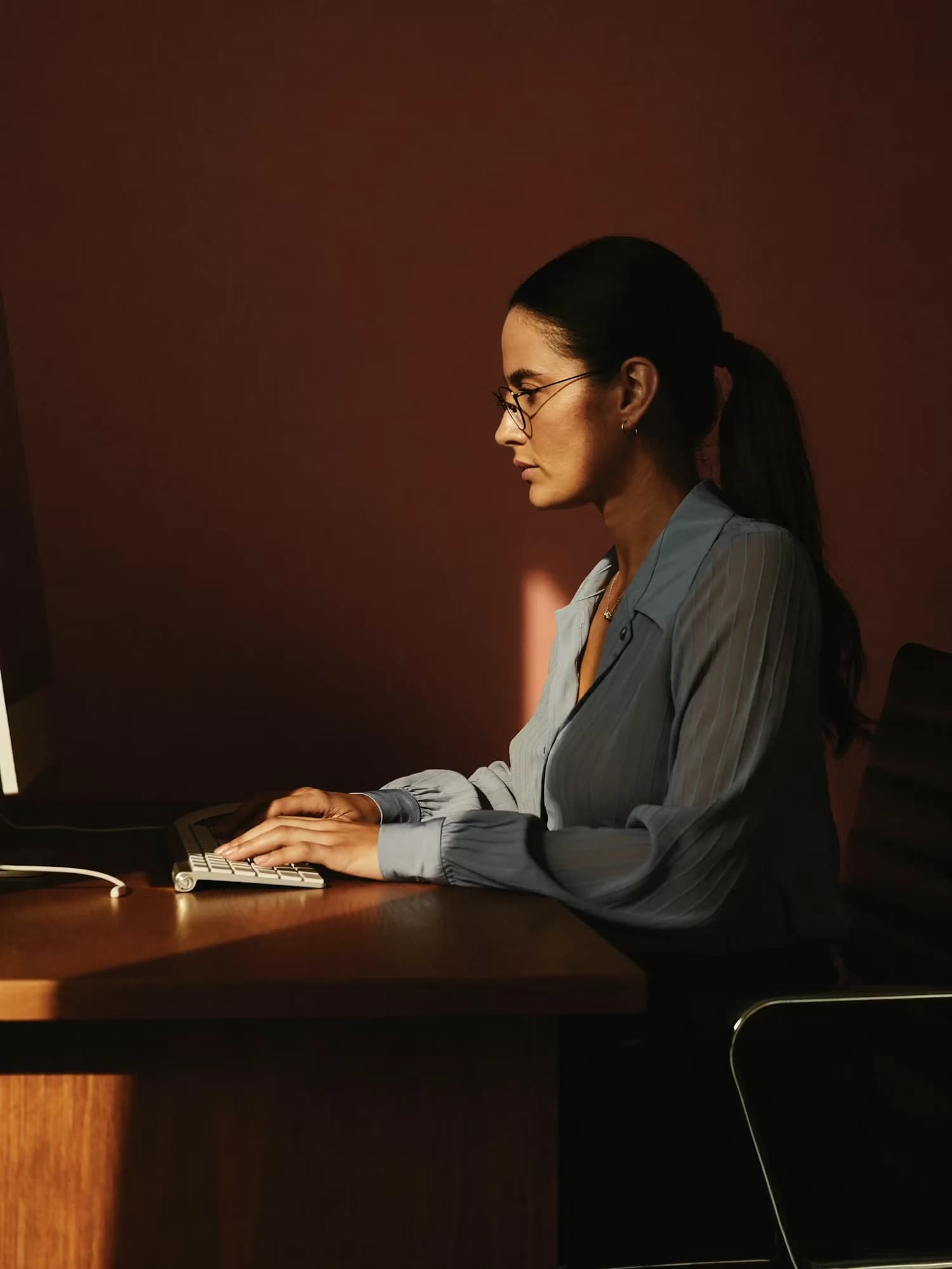 Une femme travaille sur un ordinateur de bureau dans une pièce sombre