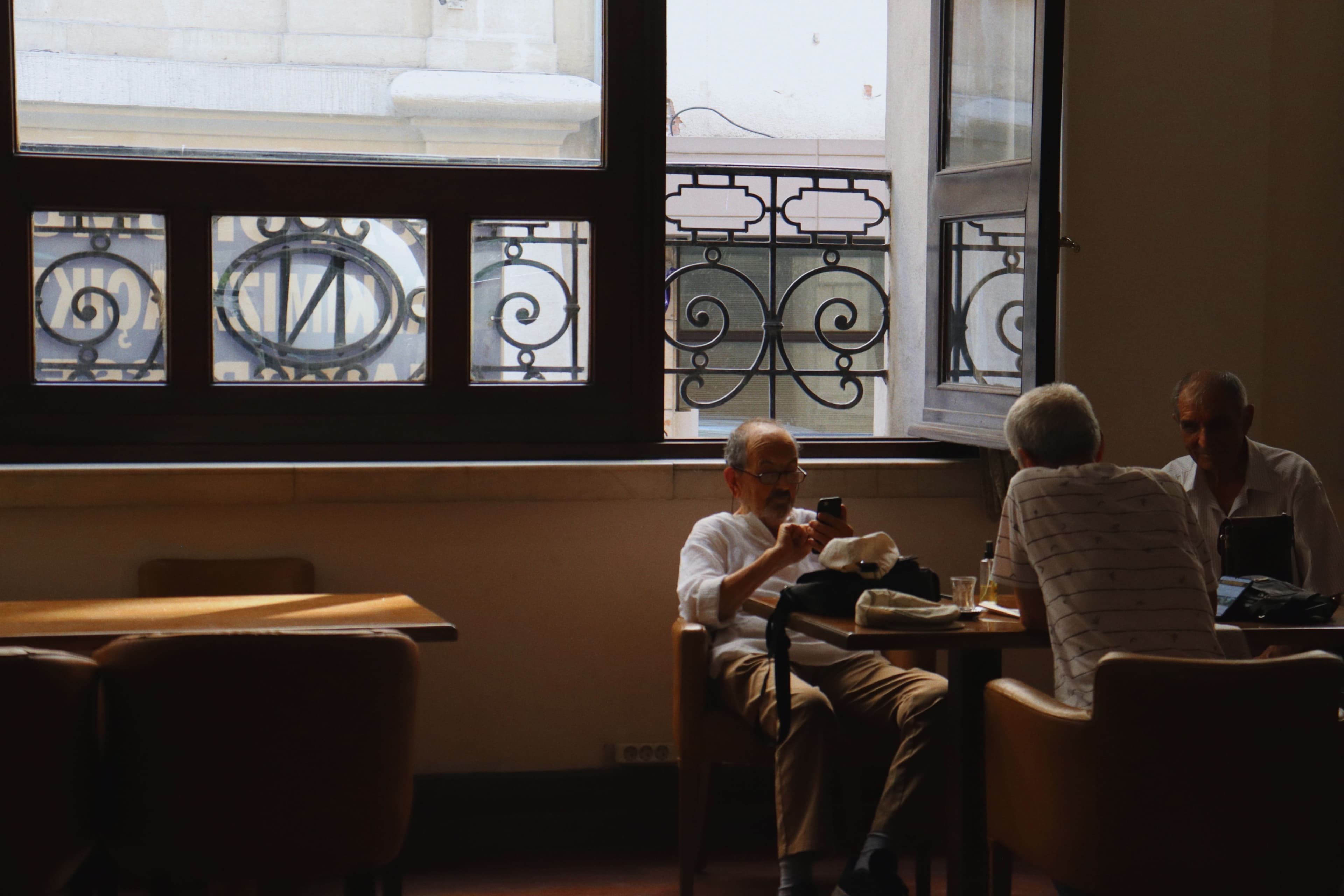 Trois hommes âgés échangent autour d’un café, dans un lieu lumineux