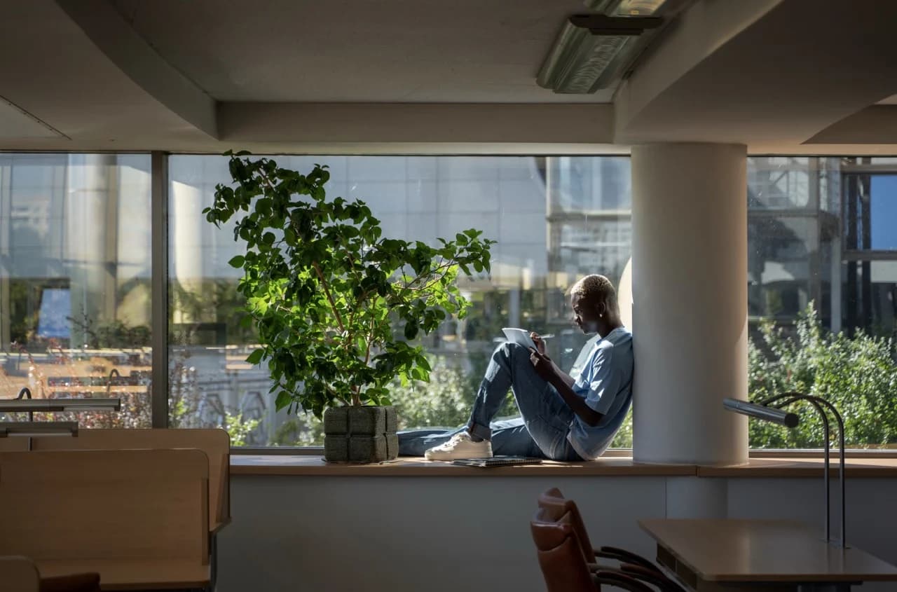 Un jeune homme assis sur le rebord d’une fenêtre, en train de lire dans un espace de travail