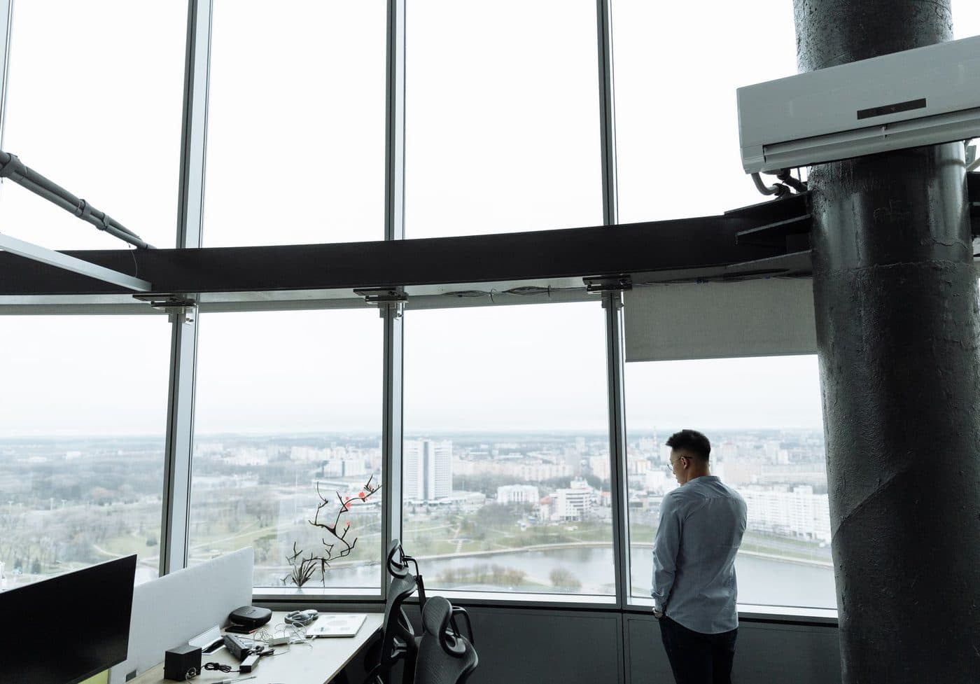Une personne de dos regarde par la fenêtre d’un bureau