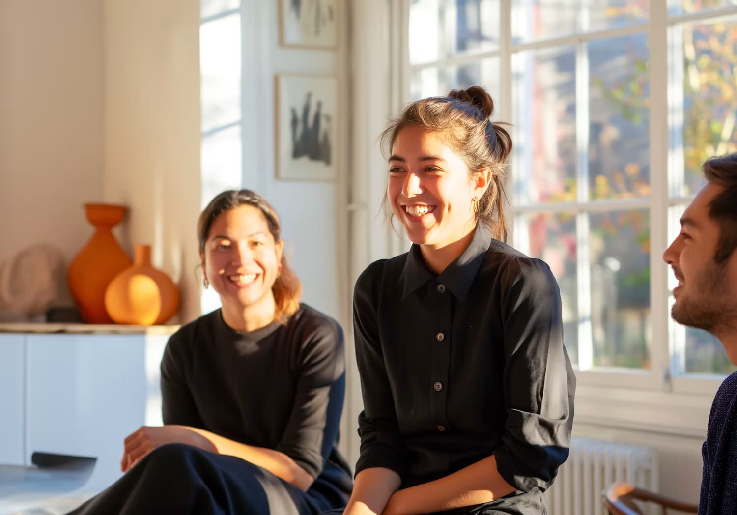 Trois collègues échangent en souriant dans un salon lumineux